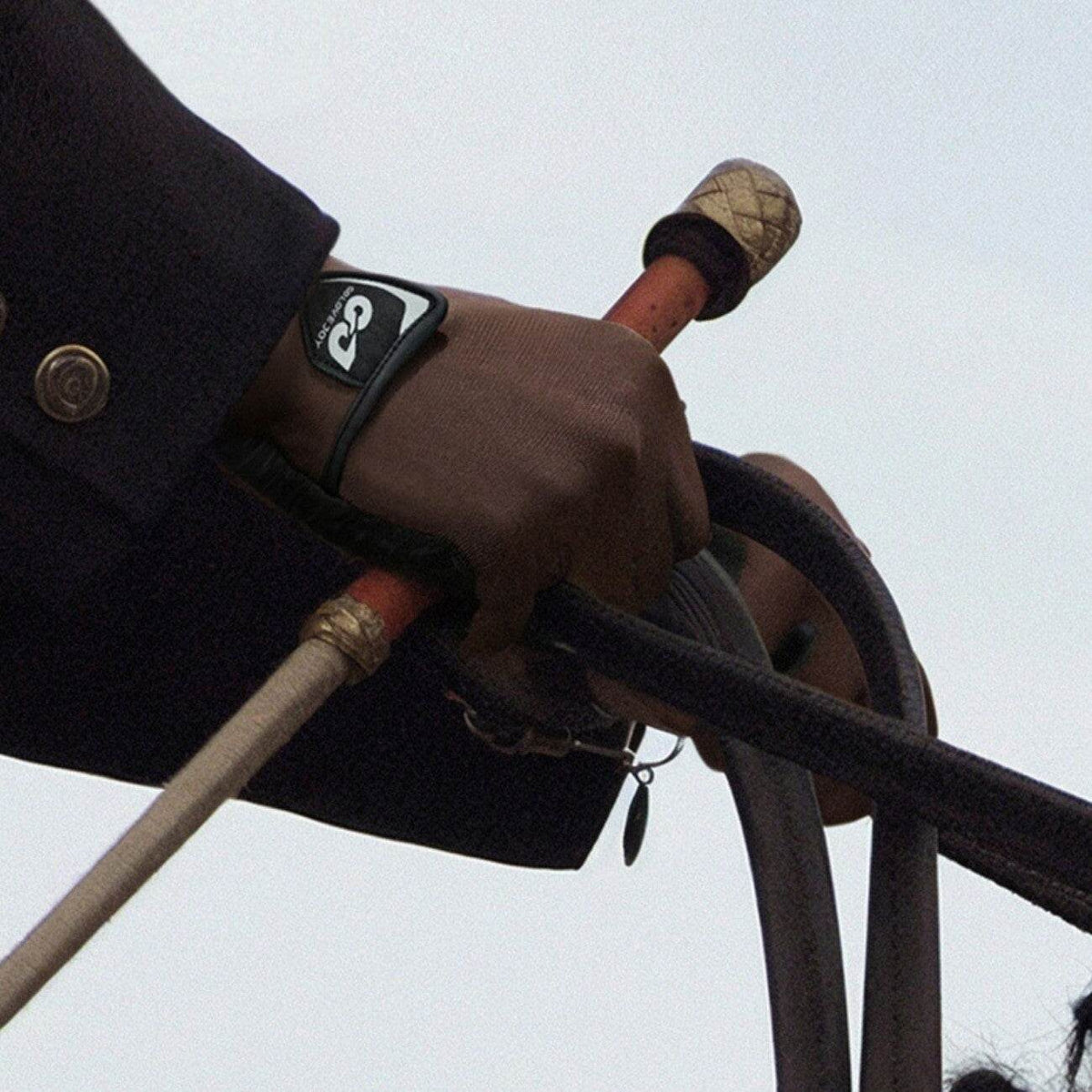 Close-up of a rider's gloved hand holding reins and a riding crop from Movagear
